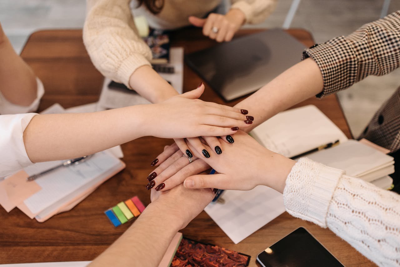 about-02 Hands stacked in teamwork gesture over a table with office items symbolizing collaboration.
