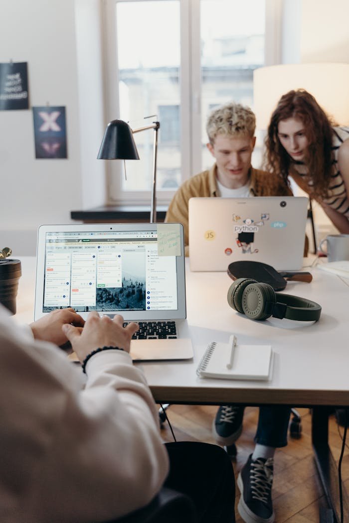 about-img Young team collaborating at a modern workspace with laptops and headphones.